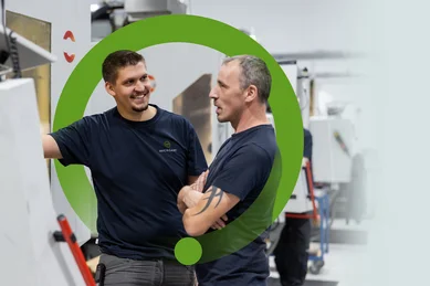 Zwei Mitarbeiter unterhalten sich an einer Fräsmaschine und lachen