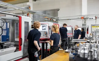 Mehrere Azubis stehen an CNC-Maschinen in der Ausbildungswerkstatt