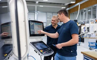 Zwei Mitarbeiter im Drehen stehen vor einen CNC-Drehmaschine. Einer davon bedient die Maschinensteuerung.