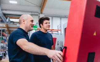 Ein Ausbilder und ein Azubi stehen vor einer CNC-Fräsmaschine