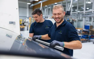 Ein Mitarbeiter im Drehen legt eine Materialstange in einen Stangenlader, der an die Drehmaschine angebunden ist