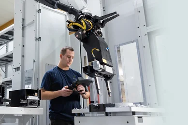 Ein Mitarbeiter im Fräsen steht neben einem Roboterarm in einer Linearanlage