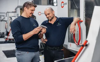 Zwei Mitarbeiter unterhalten sich an einer Fräsmaschine über ein Bauteil