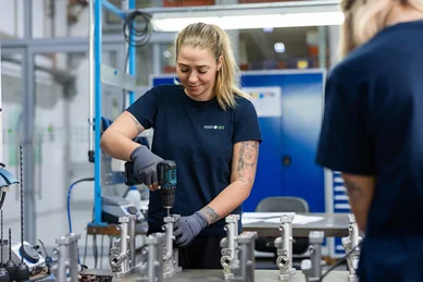 Eine Mitarbeiterin montiert ein Metallbauteil