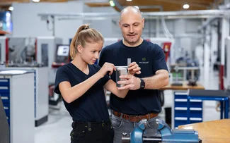 Der Ausbilder hilft einer Auszubildenden ein Bauteil zu messen