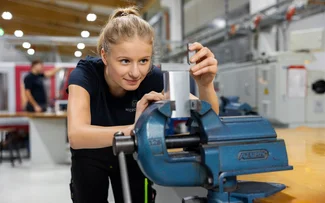 Ein Auszubildende steht am Schraubstock und bearbeitet ein Metallstück