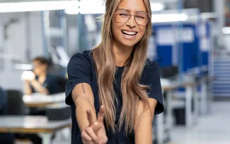 Eine grinsende Produktionsmitarbeiterin zeigt mit ihren Fingern ein Peace-Zeichen