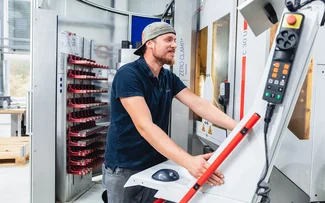 Ein Mitarbeiter im Fräsen steht an der Maschinensteuerung einer CNC-Fräsmaschine, an der ein Beladeroboter angebunden ist
