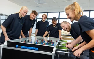 Sechs lachende Azubis spielen gemeinsam Tischkicker